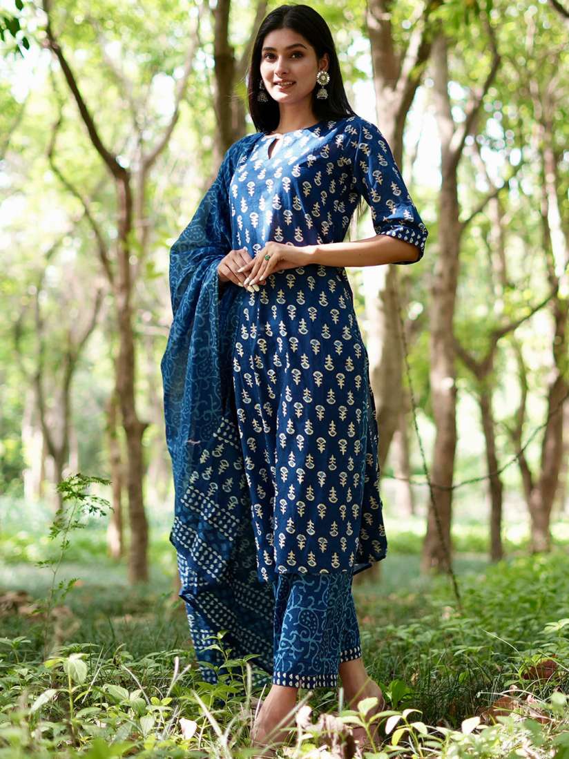 Woman wearing a blue printed kurta set with matching dupatta and trousers, posing gracefully in a green forest background